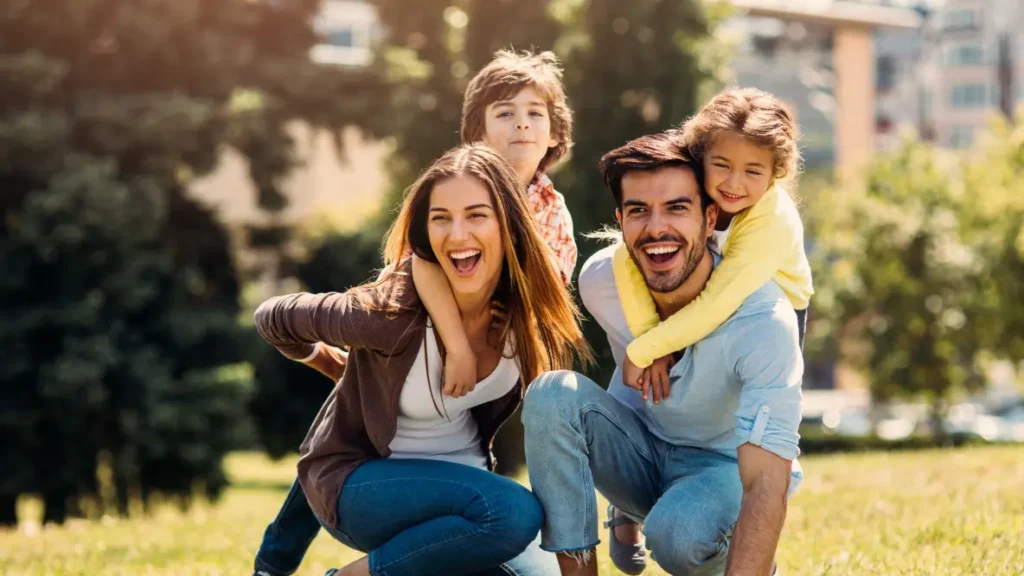 svg+xml;charset=utf em Maximídia - Seguro de Acidentes Pessoais e Seguro de Vida com o Máximo de Benefícios Casal com dois filhos brincando em uma área verde para ilustrar o artigo da Maximídia sobre seguro de acidentes pessoais