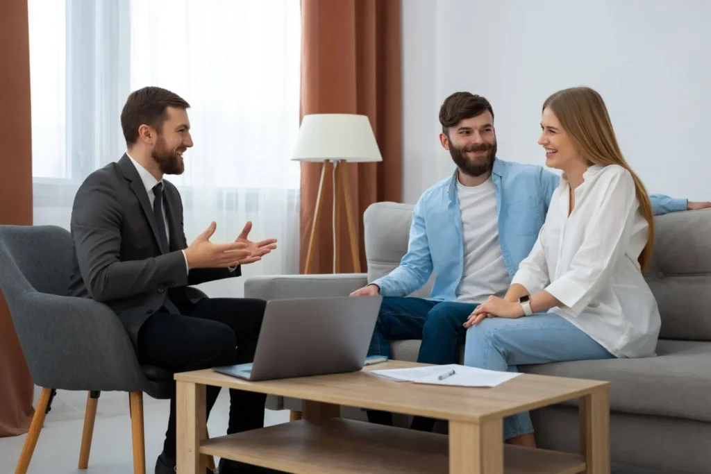 svg+xml;charset=utf em Maximídia - Seguro de Acidentes Pessoais e Seguro de Vida com o Máximo de Benefícios Consultor conversa com casal em sala de estar, durante reunião particular com notebook e documentos sobre planejamento financeiro e orientação de seguro de vida. Entenda como funciona o seguro de vida.