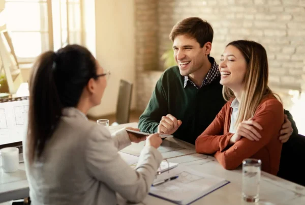 Corpo de consultor e casal sorridente em reunião à mesa com contrato e tablet, discutindo seguro e proteção financeira em ambiente residencial. seguro de vida e acidentes pessoais