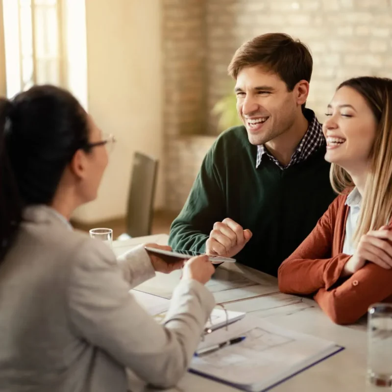 Corpo de consultor e casal sorridente em reunião à mesa com contrato e tablet, discutindo seguro e proteção financeira em ambiente residencial. seguro de vida e acidentes pessoais